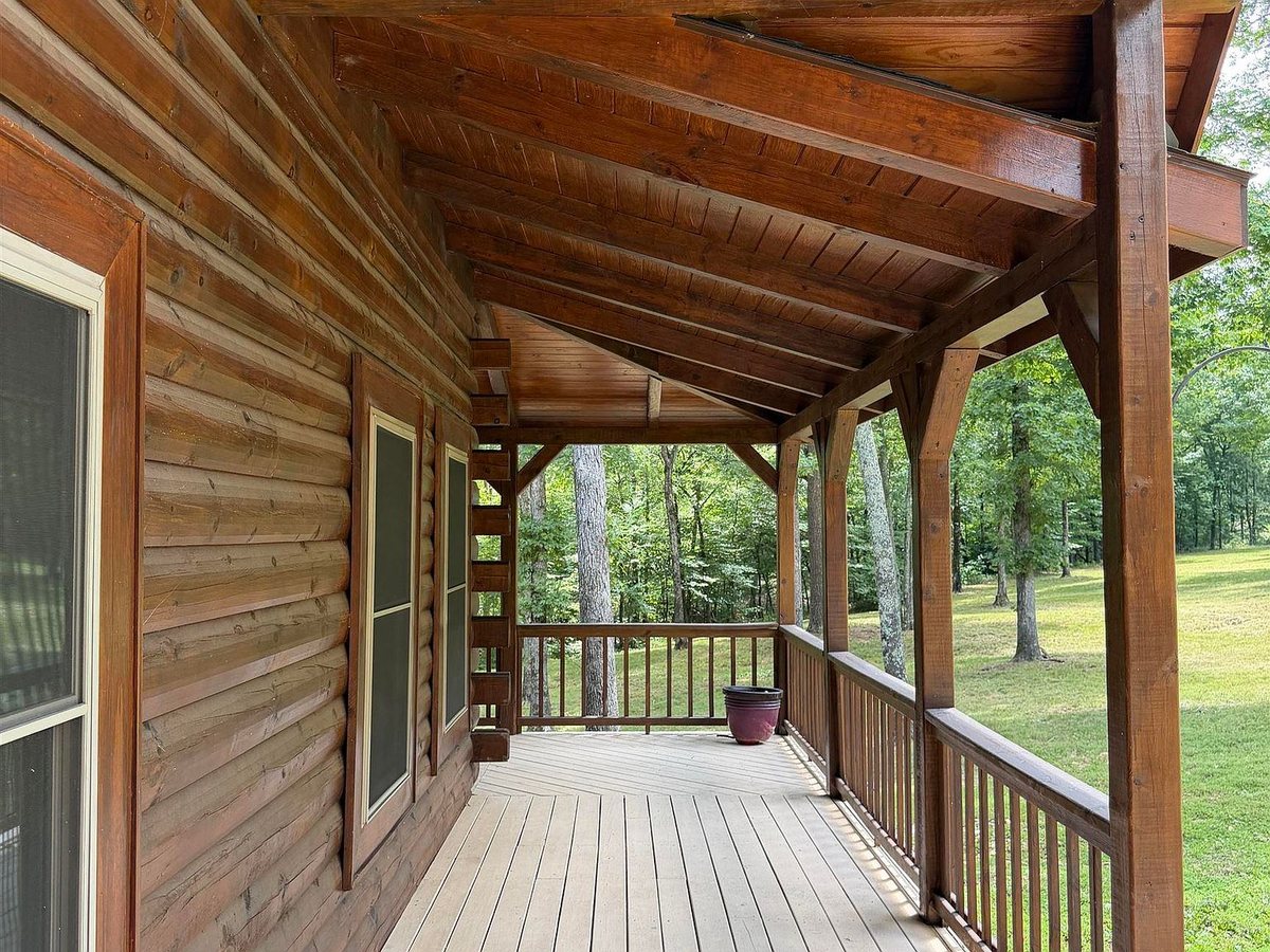 Covered wraparound porch of Sugar Creek Cabin with timber-frame rafters, log walls and the forest beyond